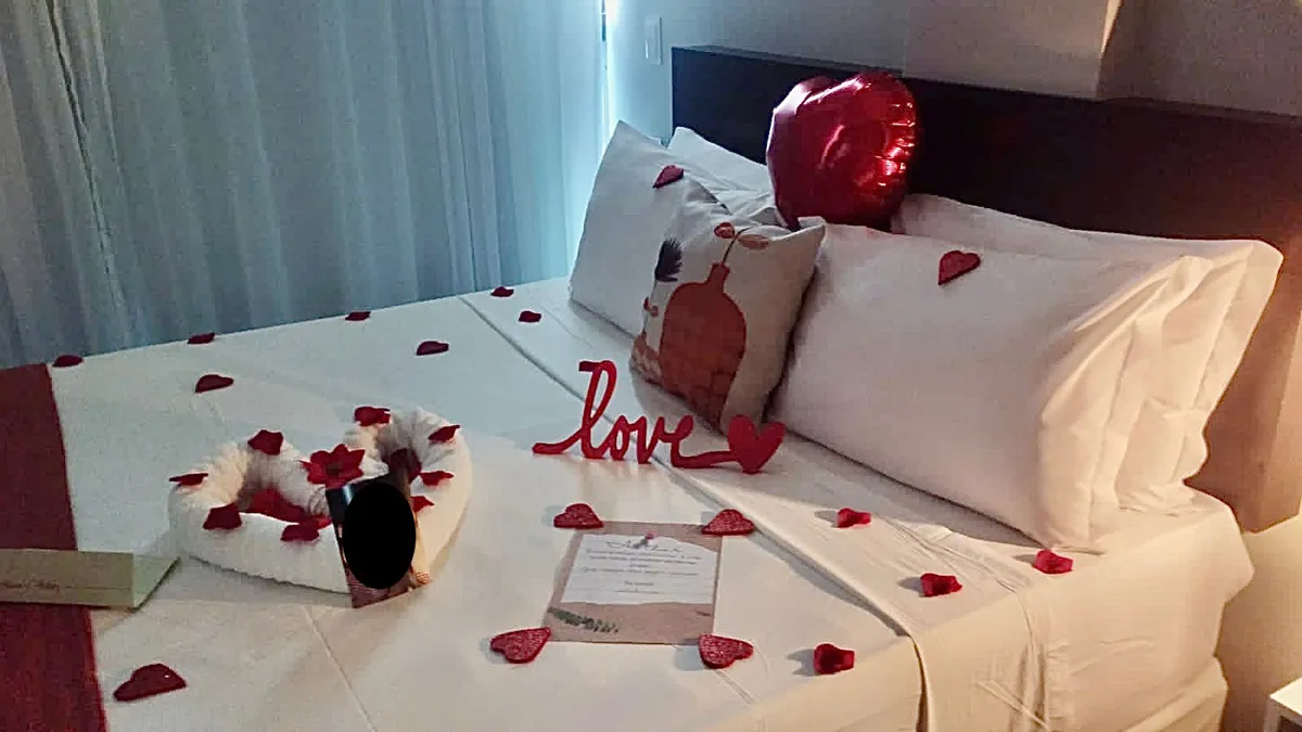Cama decorada com pétalas de rosas, balão de coração e cartão romântico